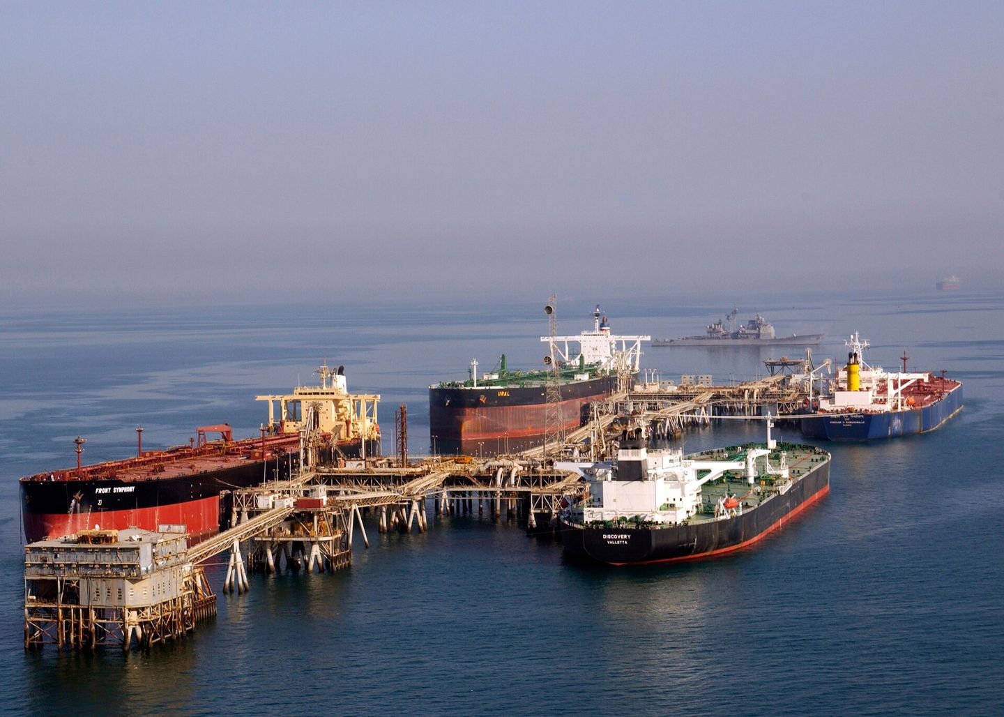 Three crude tankers moored at an offshore loading terminal in the Gulf, a warship on the horizon.