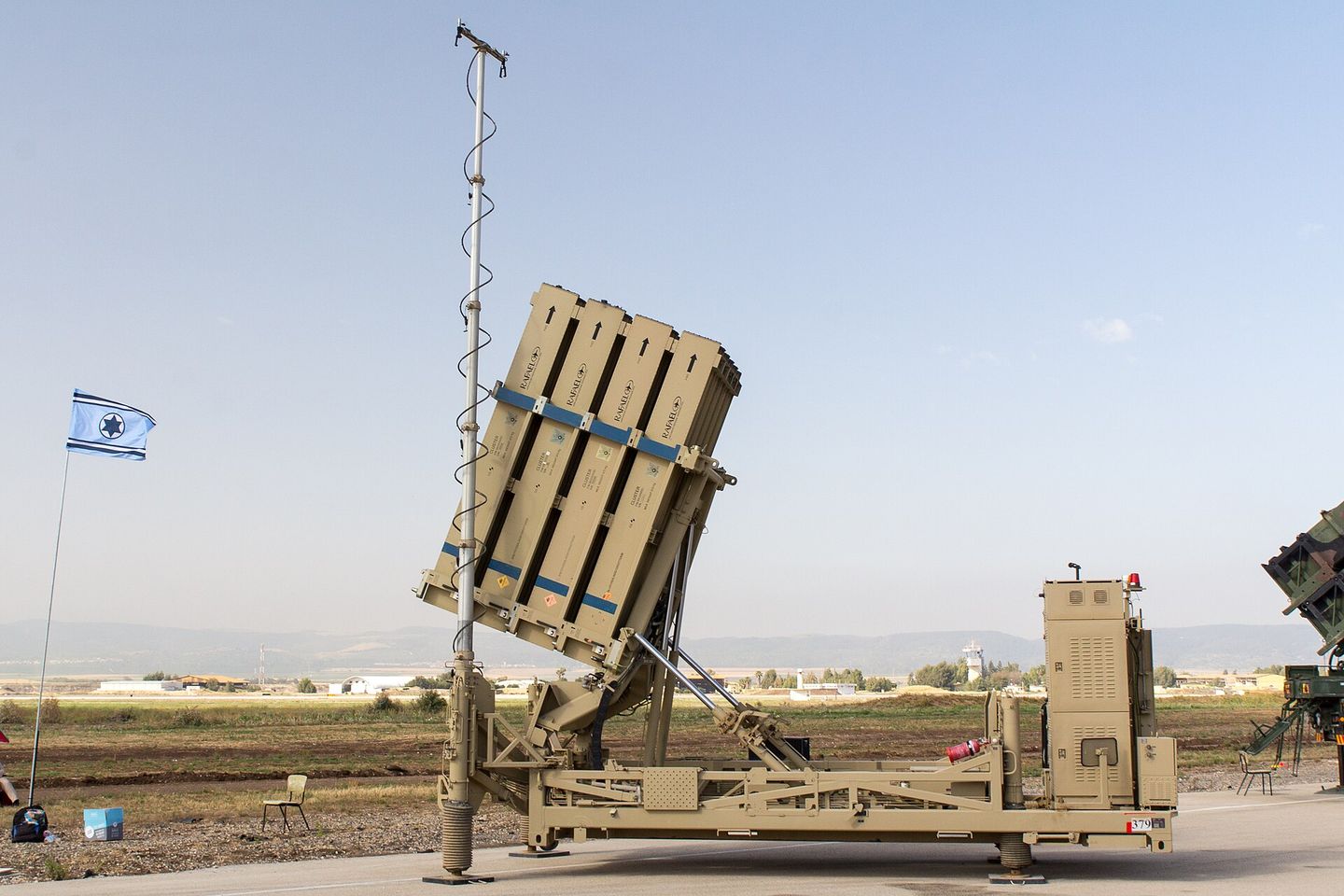 An Iron Dome interceptor launcher raised on an apron, an Israeli flag flying beside it.