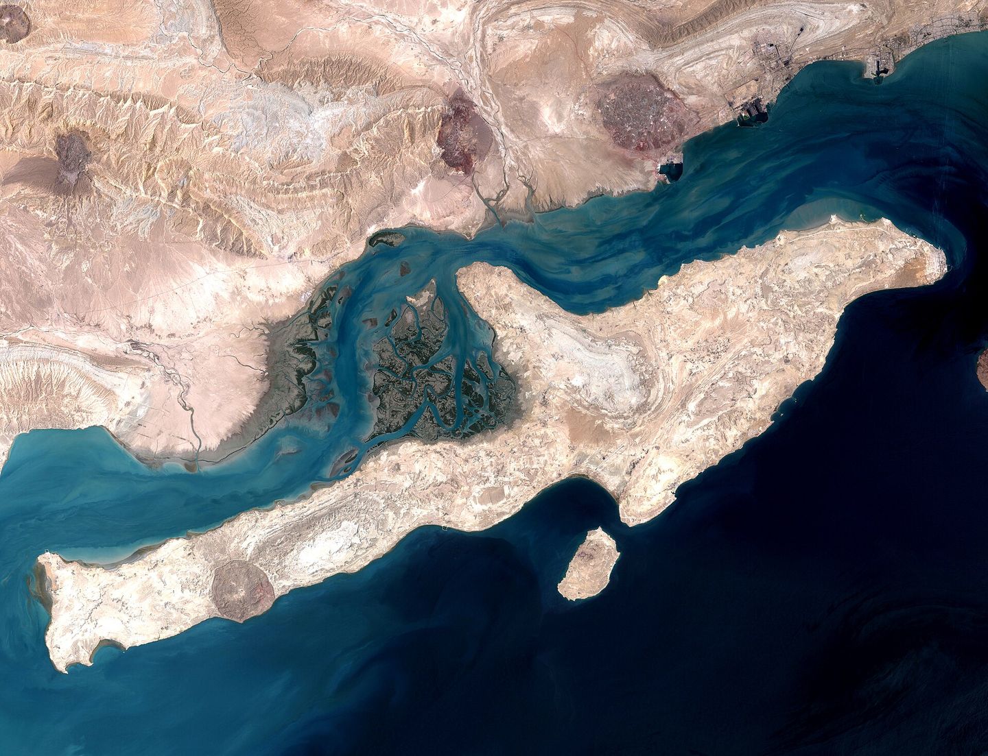 A satellite view of Qeshm Island in the Strait of Hormuz, the deep-water channel running dark between the island and the Iranian coast.