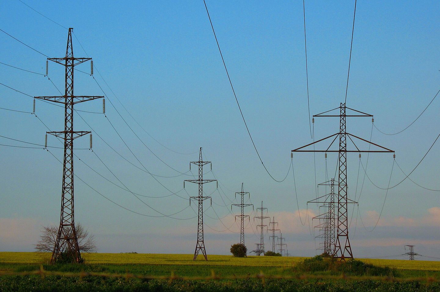 A line of high-voltage transmission towers carrying overhead conductors across open farmland.